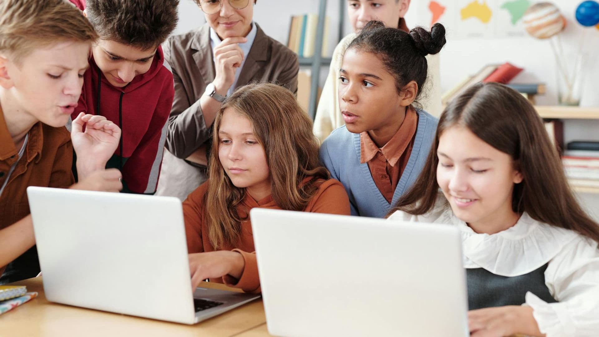 Teenage students actively collaborate on laptops in an educational environment with guidance from a teacher.