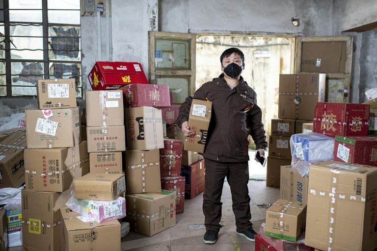 Delivery worker holding packages in a Wuhan warehouse, wearing a face mask.